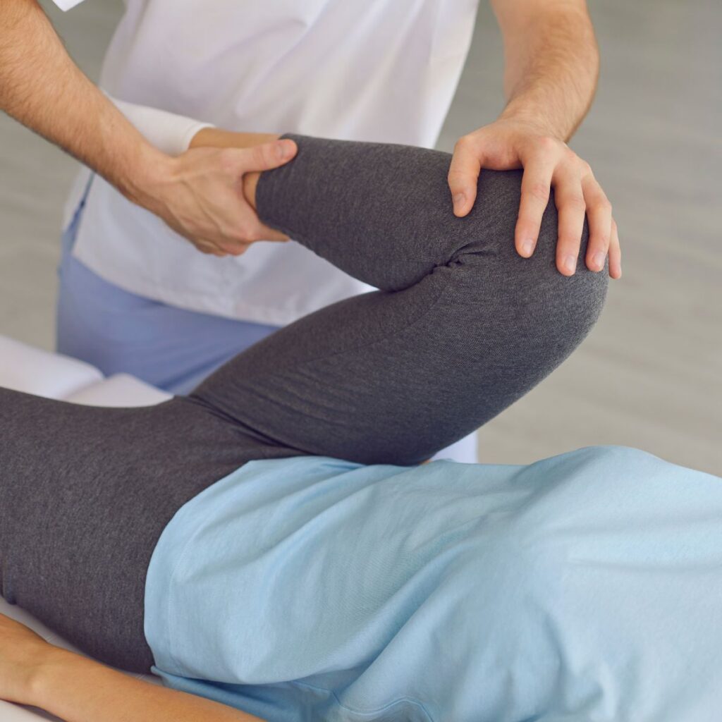 A physical therapist performs a hip stretch on a patient lying on a treatment table.
